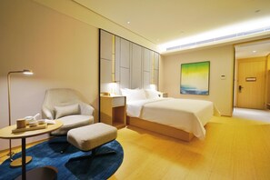 A hotel room with a bed, a chair, a small table, a nightstand, and a painting on the wall. - Ji Hotel (Suzhou)
