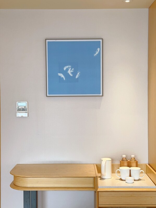 Habitación con una obra de arte enmarcada de pájaros, un termostato pequeño y una mesa de madera con una taza blanca y dos botellas.