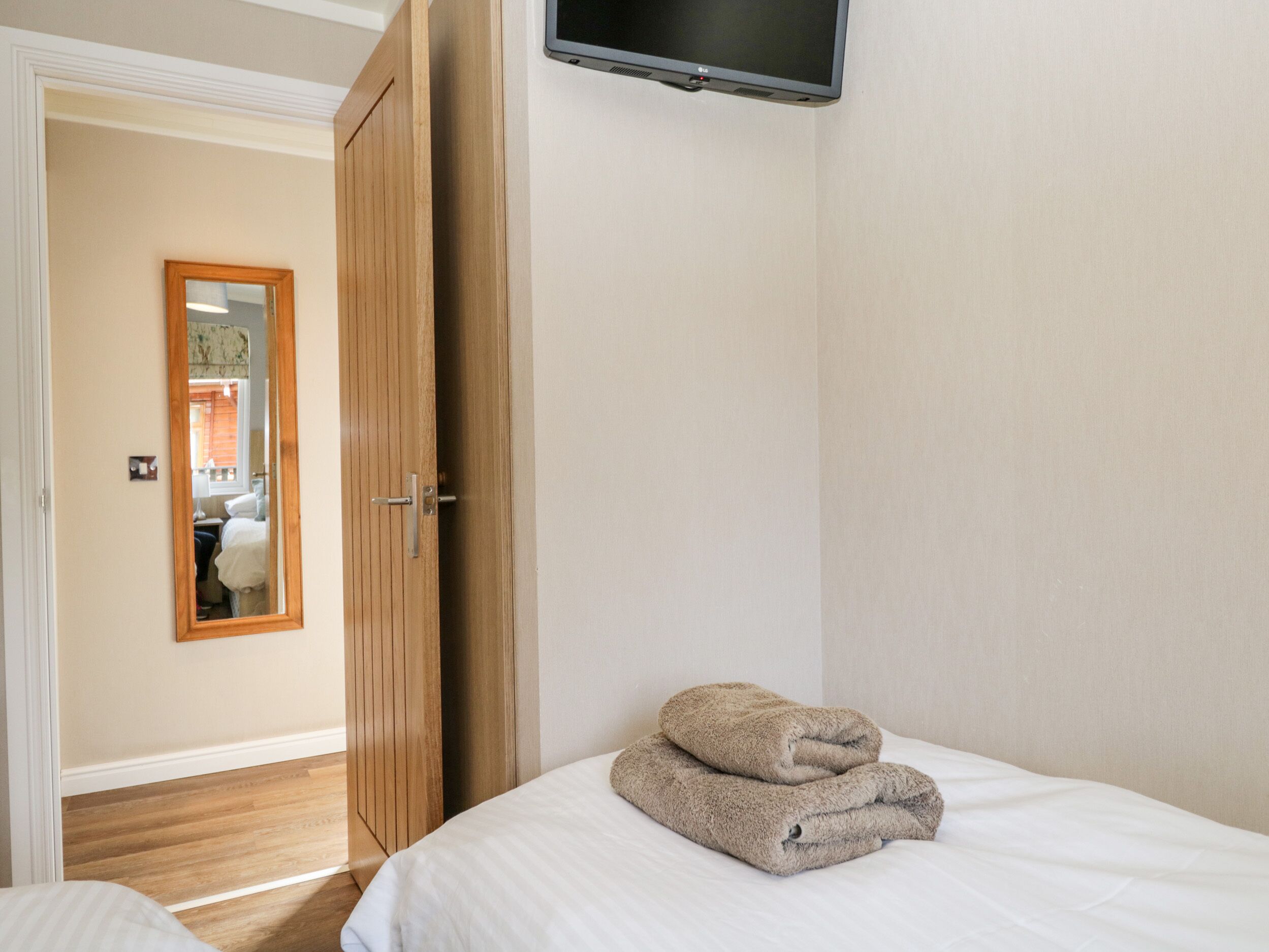 A hotel room with a bed, a wooden wardrobe, a mirror, and a television on the wall.