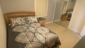 A bedroom with a bed, nightstand, dresser, and a mirror.