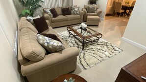 A living room with beige sofas, a glass coffee table, and a patterned rug.