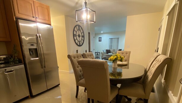 A modern kitchen with stainless steel appliances, a dining area with a round table and chairs, and a large wall clock.