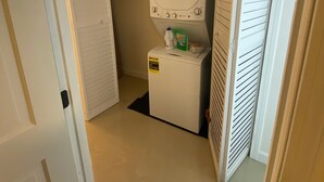 A compact laundry room with a front-loading washer and dryer, a small shelf with cleaning supplies, and a vented dryer.