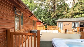 Una cabaña de madera con jacuzzi, terraza y vistas al bosque circundante.