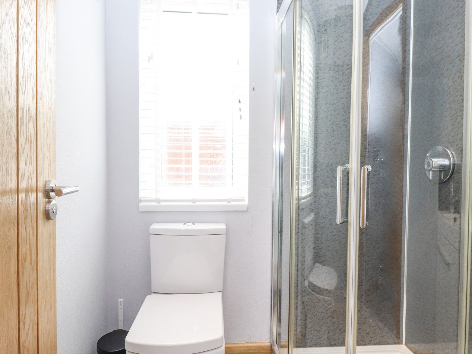 Une salle de bain comprenant des toilettes, une douche en verre et une fenêtre avec des stores.
