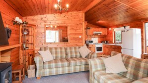 Ein gemütliches Cabin-Interieur mit einer karierten Couch-Garnitur, einer Holzbalkendecke und einer Küchenzeile mit Kühlschrank und Herd.