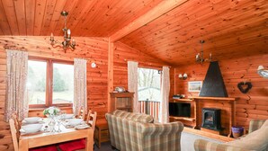 Ein gemütliches Cabin-Interieur mit Esstisch für vier Personen, einer Karo-Sofa, einem Fernseher und einem Kamin.