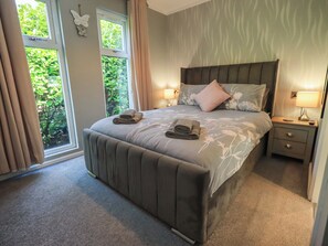 A bedroom with a bed, two bedside tables, a window with curtains, and a view of greenery outside.