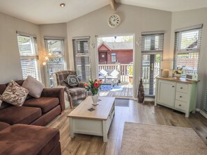 A cozy living room with a brown sofa, a plaid armchair, a wooden coffee table, and a view of the outside deck.
