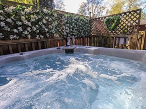 A hot tub surrounded by a wooden fence with flowering plants.