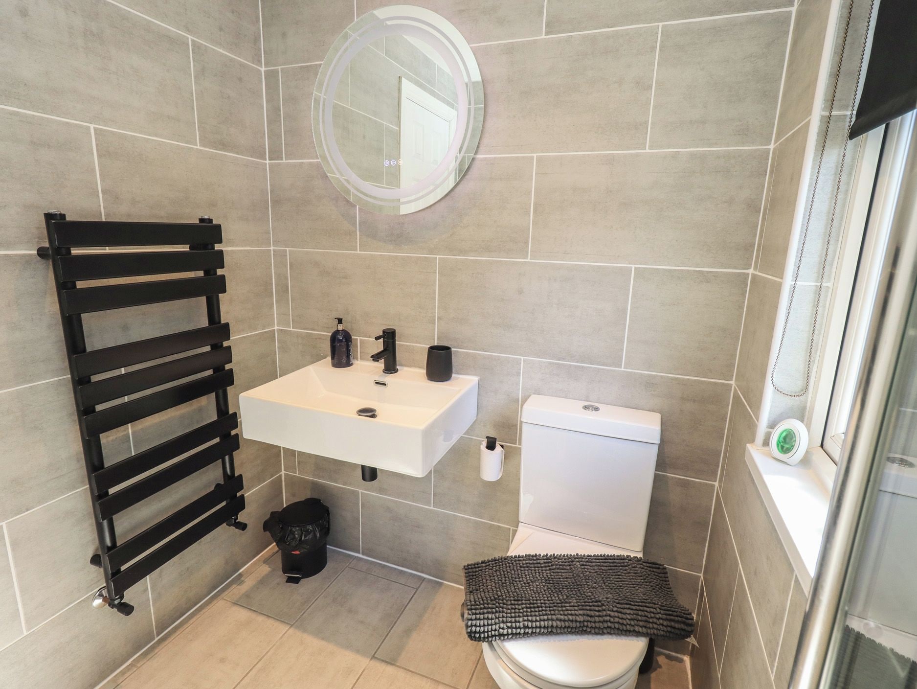 A bathroom with a white sink, black towel rack, toilet, and a mirror.