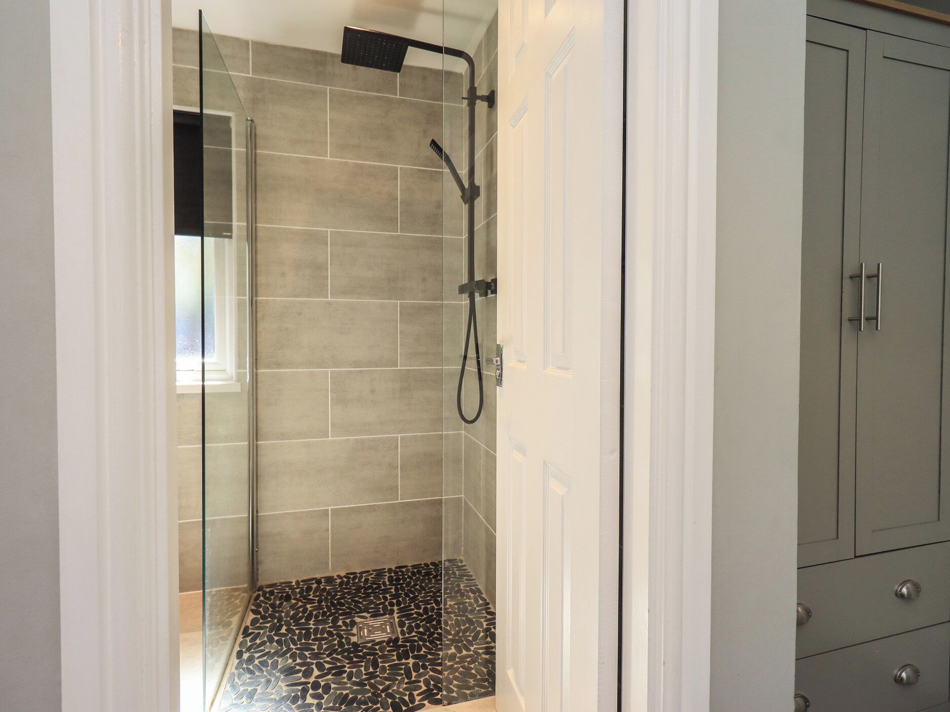 A shower with a glass door, tiled walls, and a pebble-patterned floor.