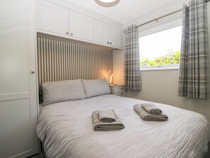 A bedroom with a bed, pillows, a nightstand, a window with curtains, and a wall with vertical blinds.