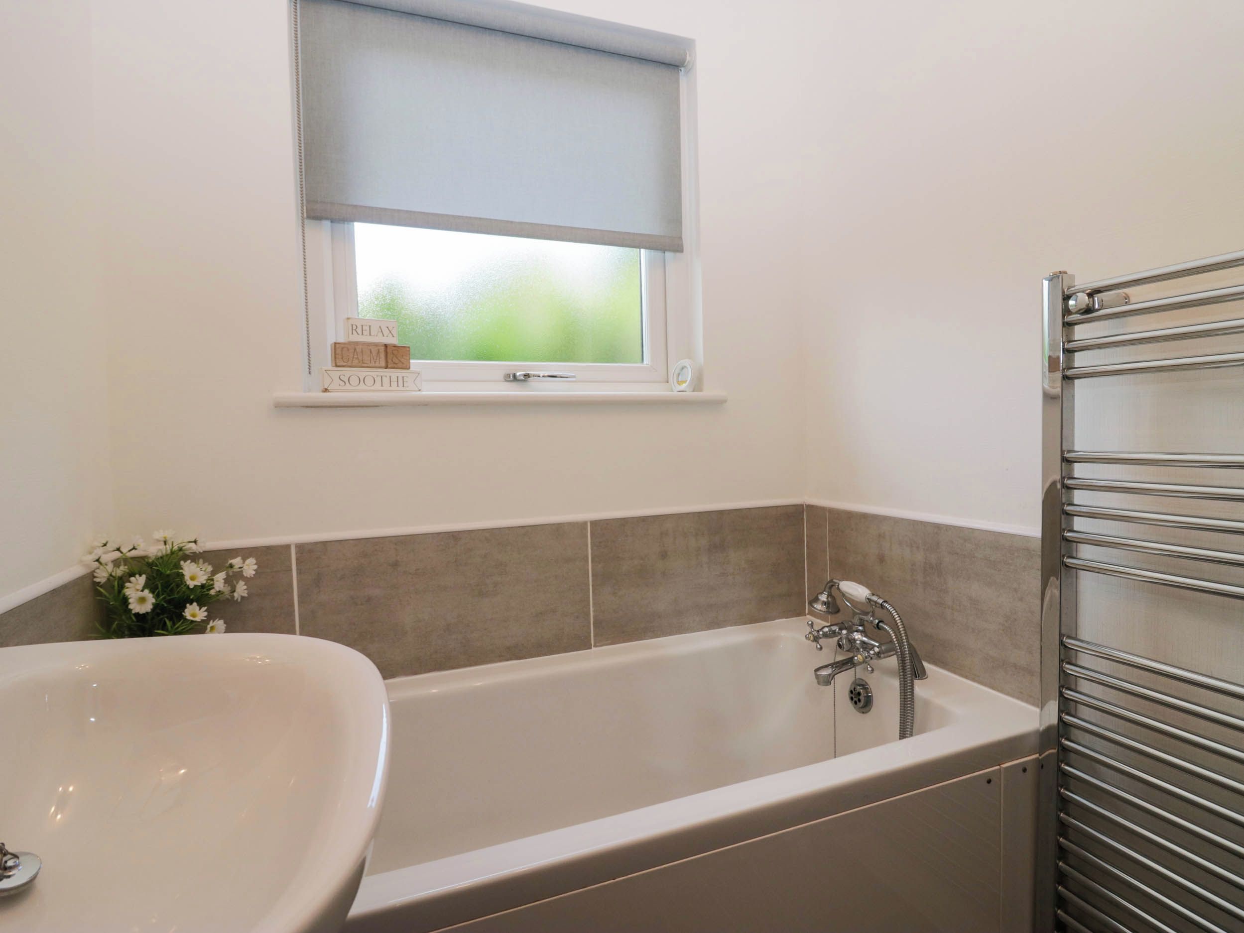 A bathroom with a freestanding bathtub, a window with a blind, and a towel rack.