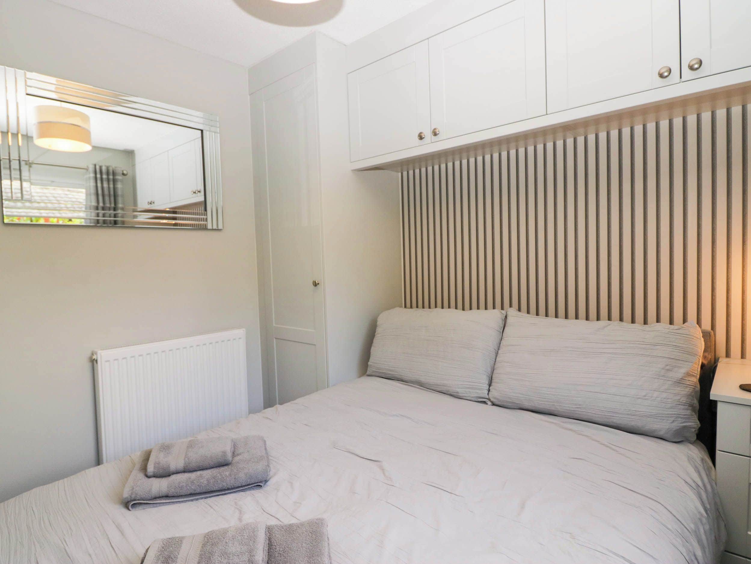 A bedroom with a bed, a radiator, a mirror, and a wardrobe.