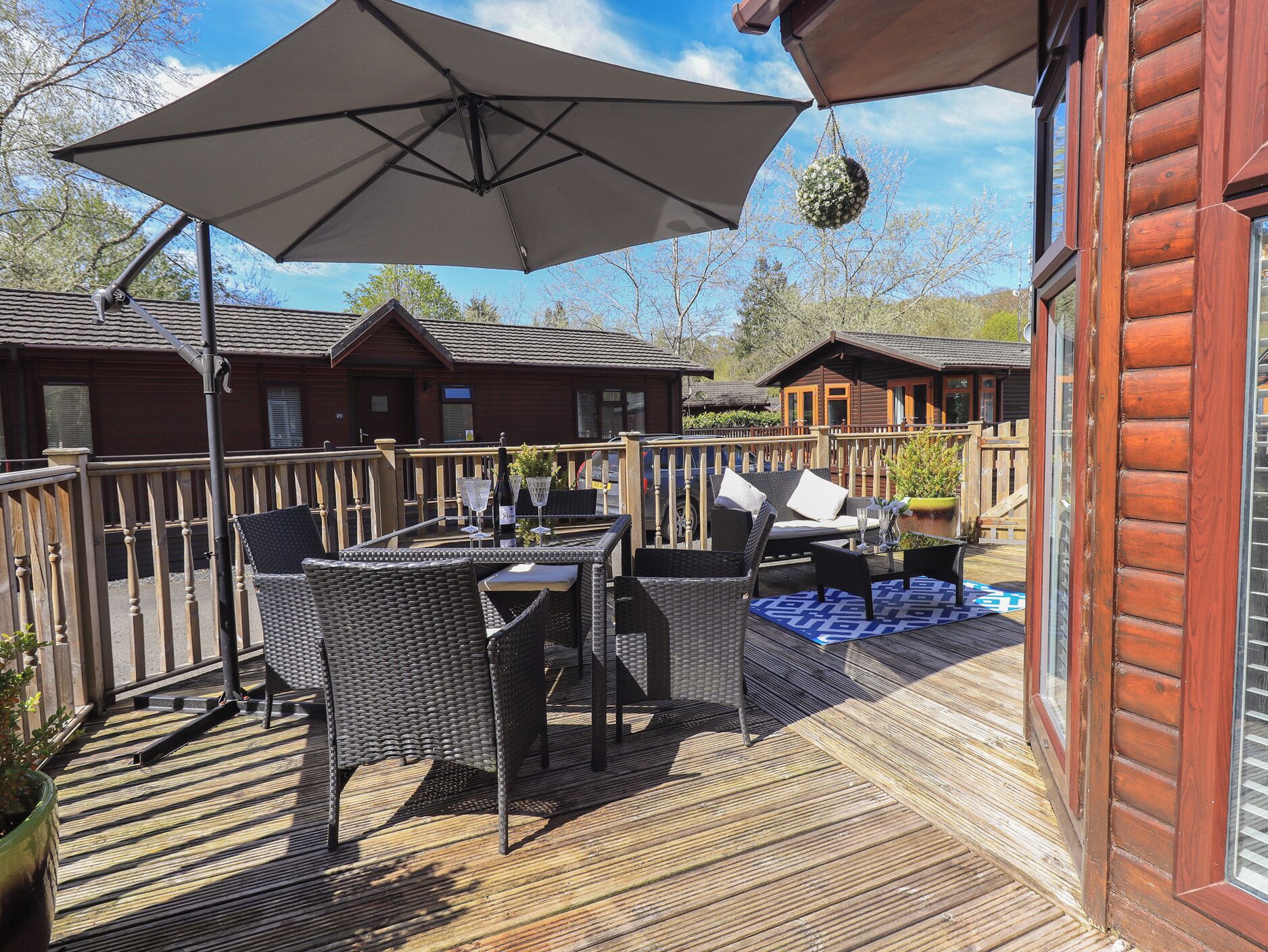 A wooden deck with outdoor furniture, a table with a bottle and glasses, and a hanging ornament.
