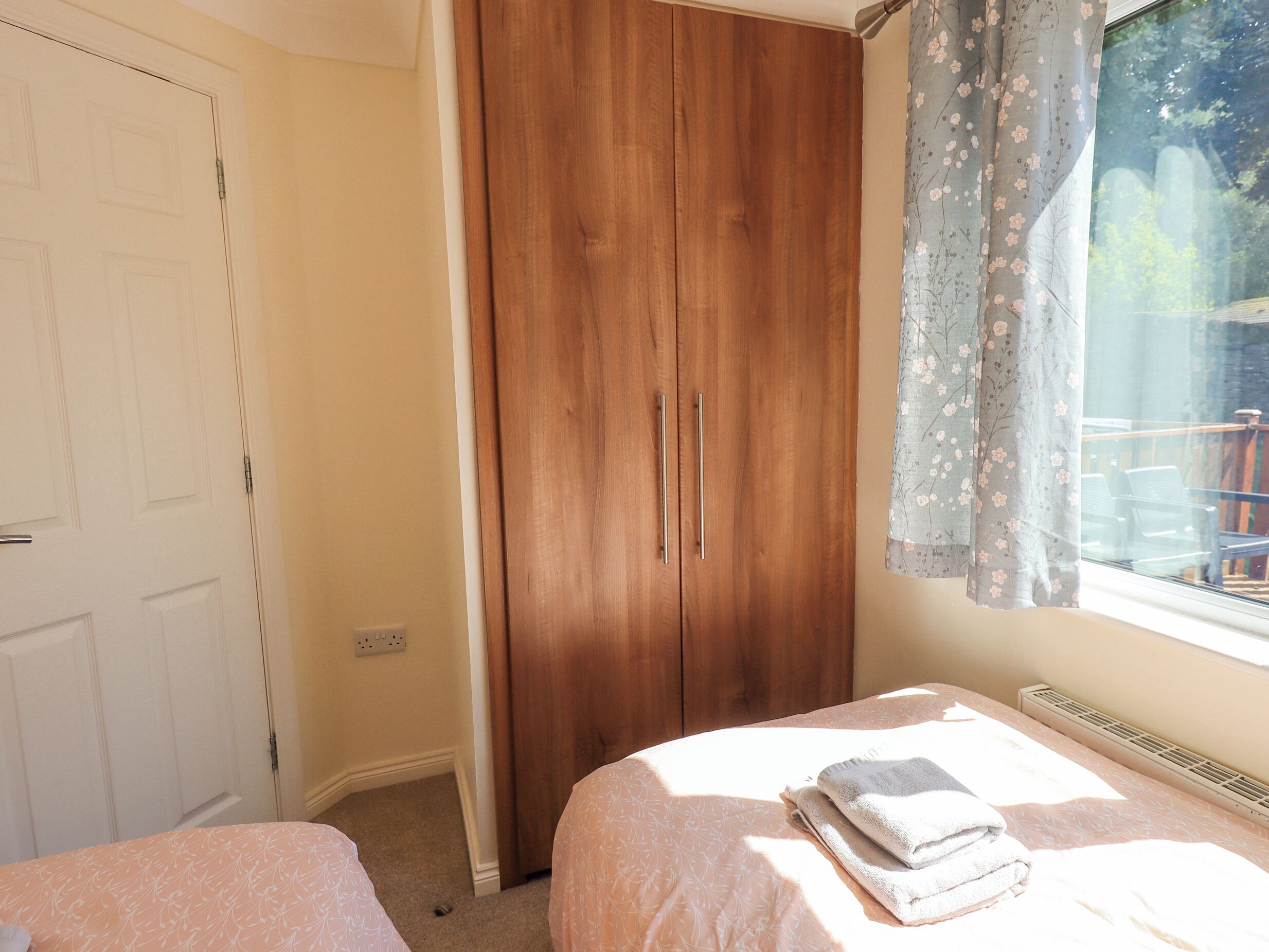 A bedroom with two beds, a wooden wardrobe, and a window with floral curtains.