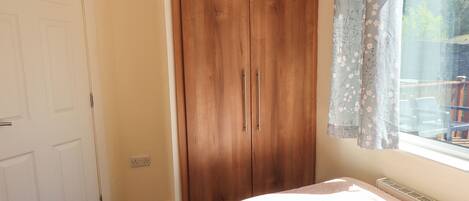 A bedroom with two beds, a wooden wardrobe, and a window with floral curtains.