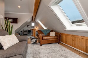 Relax in this cozy attic room with a panoramic view of the surrounding landscape, featuring a comfortable sofa and a wooden floor.