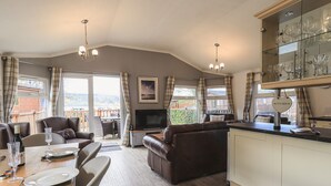 A modern living room with a sofa, dining table, and kitchen area. - Sunny Brow Lodge (Windermere)