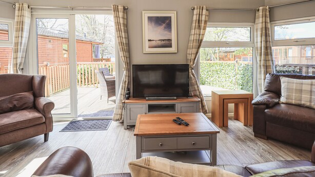 A cozy living room with a TV, comfortable seating, and a view of the outside. - Sunny Brow Lodge (Windermere)