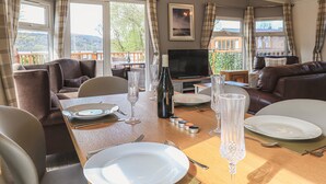 A dining area with a table set for four, a television, and a view of the outdoors. - Sunny Brow Lodge (Windermere)