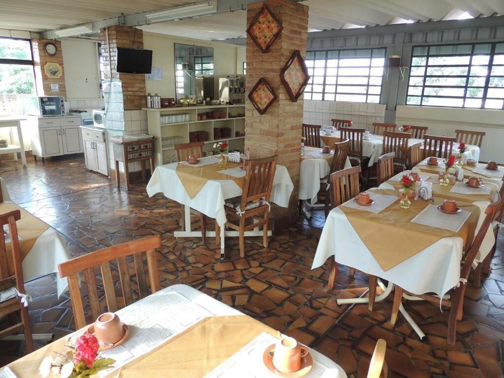 Restaurante com várias mesas, cadeiras e uma área de cozinha.