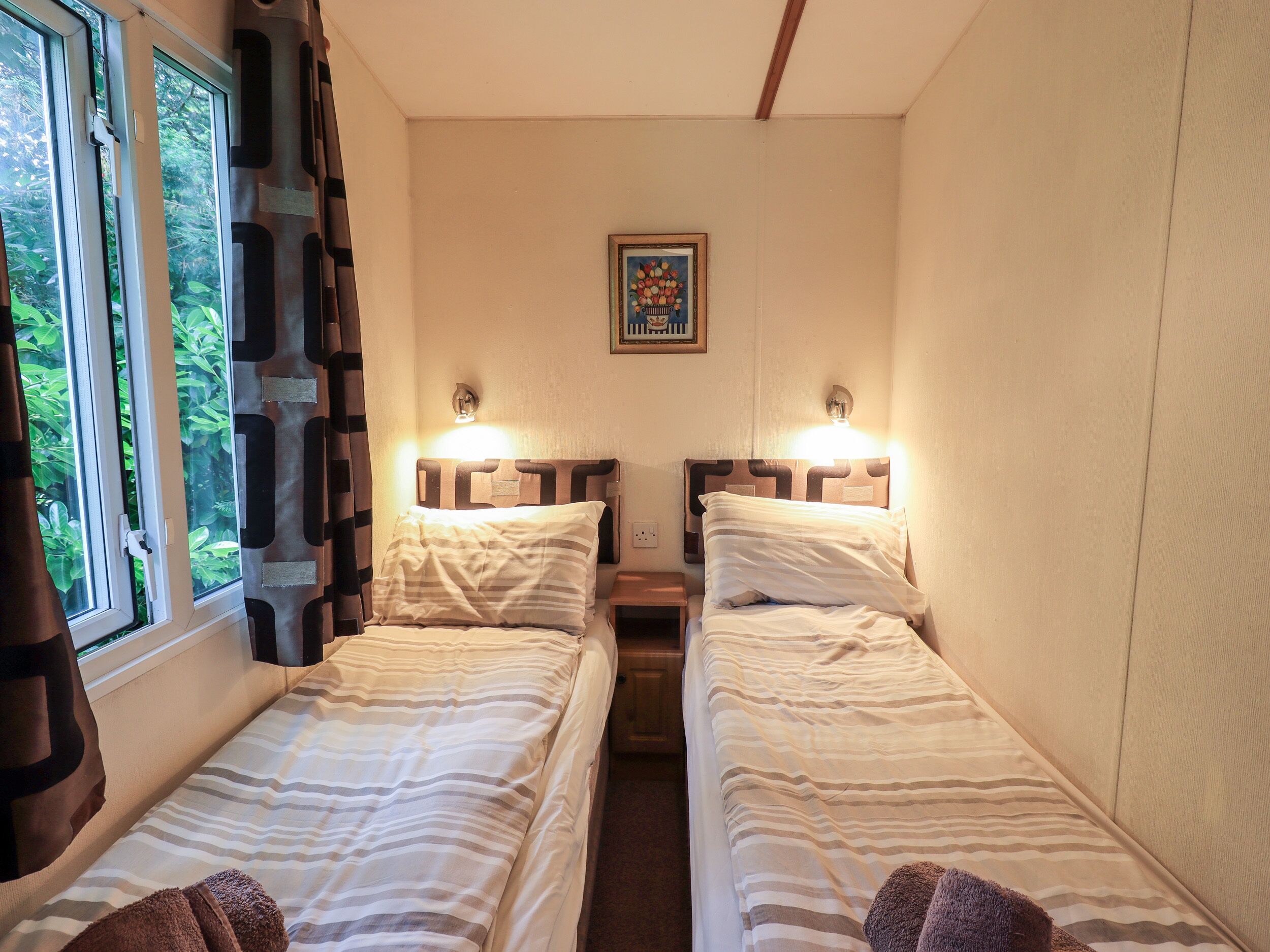 Ein kleiner, gemütlicher Raum mit zwei Einzelbetten, einem fenster mit Vorhängen und einem gerahmten Bild an der Wand.