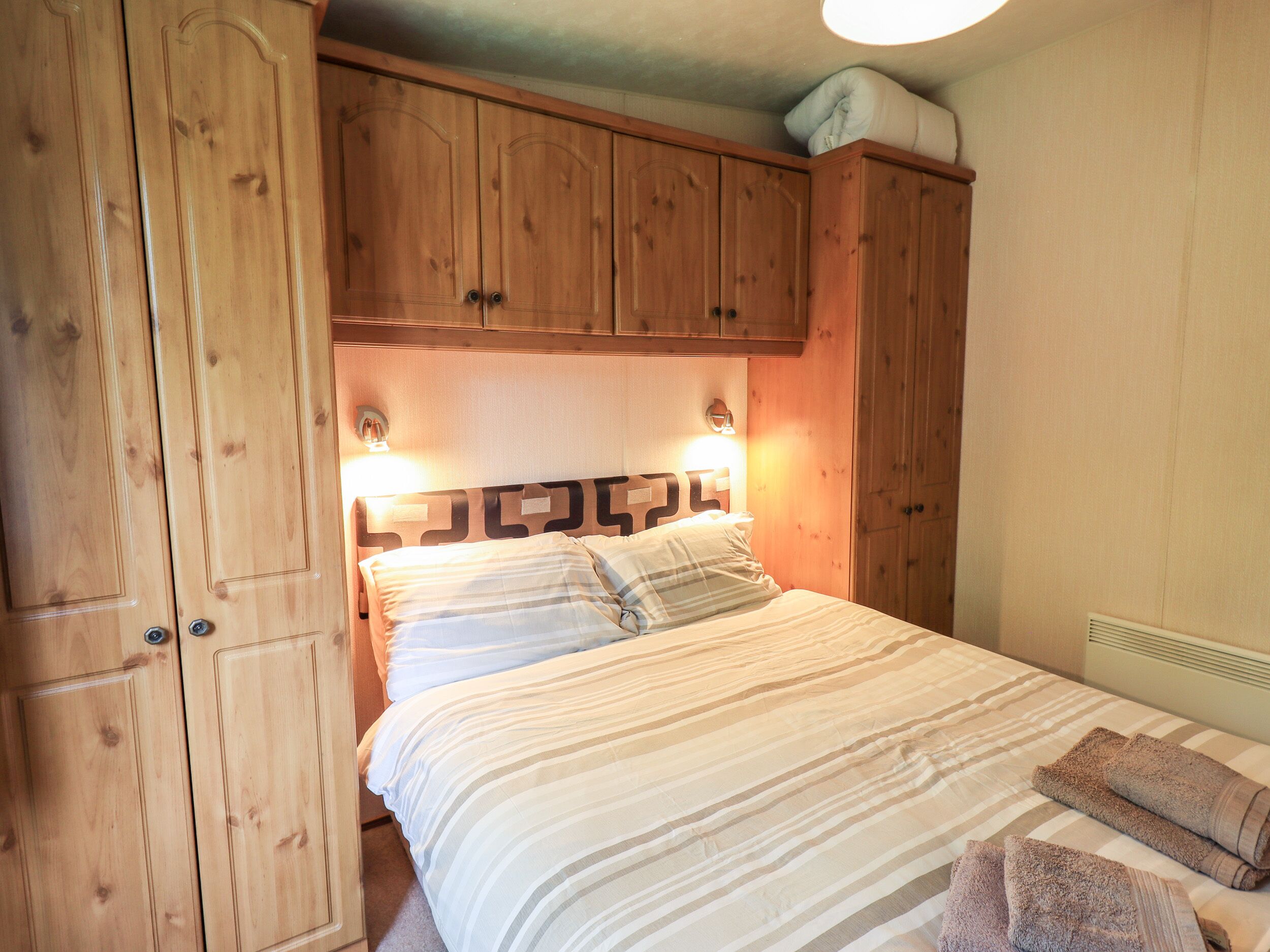 Une chambre à coucher avec un lit, une armoire en bois et une tête de lit dotée de lampes.
