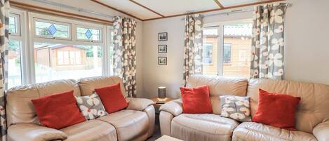 Una sala de estar acogedora con dos sofás de cuero color beige, cojines estampados en rojo y blanco, una mesa de centro de madera y una cesta decorativa.