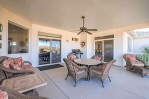 Un patio couvert aménagé avec des meubles en osier, un ventilateur de plafond et une vue sur l’extérieur.
