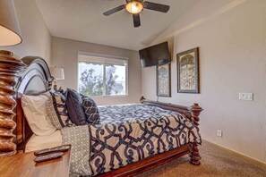 Une chambre à coucher avec un lit, un ventilateur de plafond, une fenêtre et un téléviseur fixé au mur.