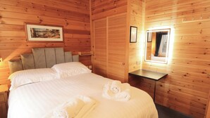 A wooden cabin-style room with a bed, a bedside table, a mirror, and a framed picture on the wall. - The Fold (Keswick)