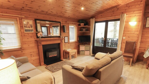 A cozy cabin interior with a fireplace, wooden walls, a sofa, and a television. - The Fold (Keswick)