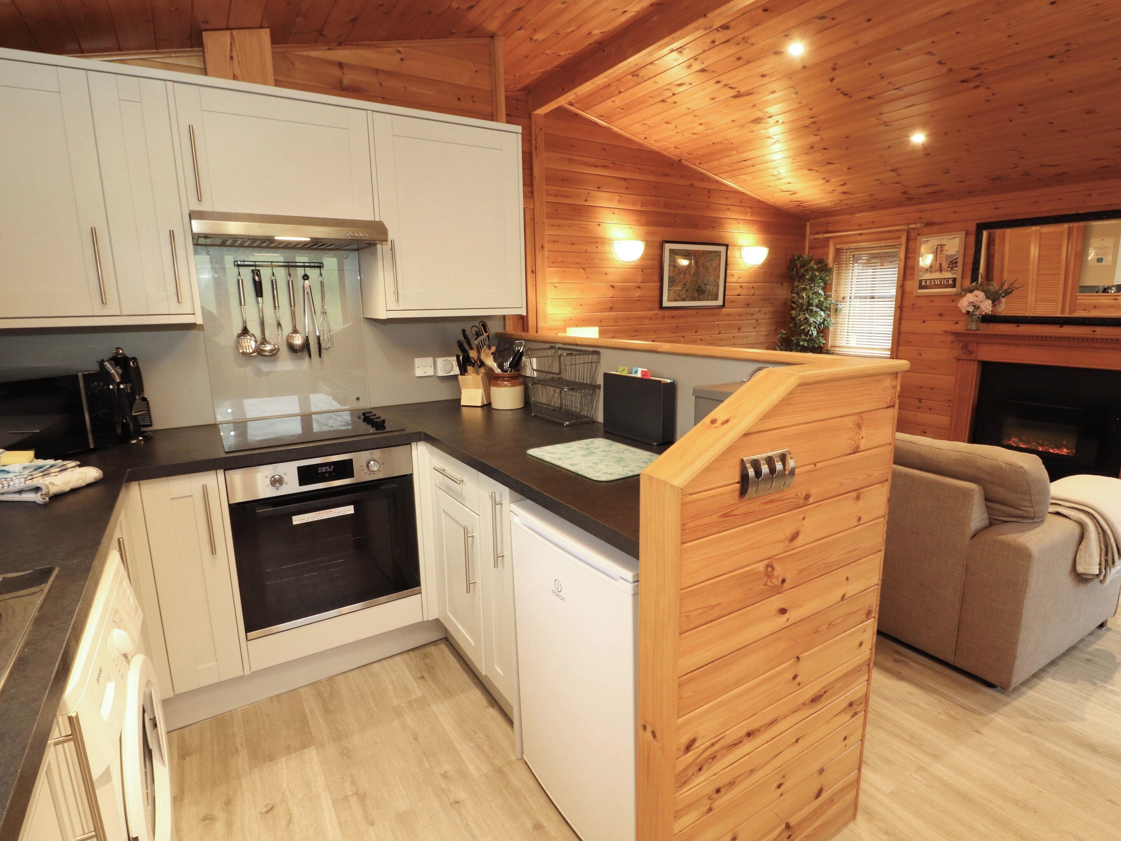 A modern kitchen with white cabinets, a black countertop, and stainless steel appliances. There is a wooden dining area with a sofa and a fireplace.