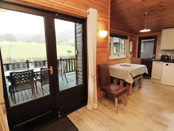 Une cabane en bois comprenant un coin repas, une cuisine et offrant une vue sur un champ verdoyant.