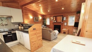 A cozy cabin-style room with a kitchenette, a fireplace, a sofa, and a dining area. - The Fold (Keswick)