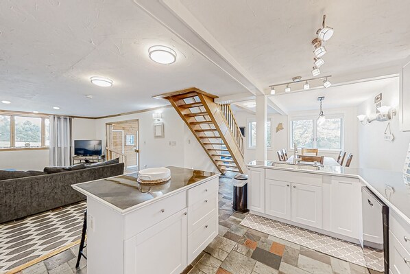 Cozy living area with a central island kitchen, wooden staircase, and large windows.