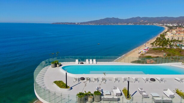 A resort pool with clear blue water, surrounded by lounge chairs and potted plants, overlooking a beach and ocean. - Amazing Jewel Beach front Condo with great views (Bucerias/ Nuevo Vallarta)