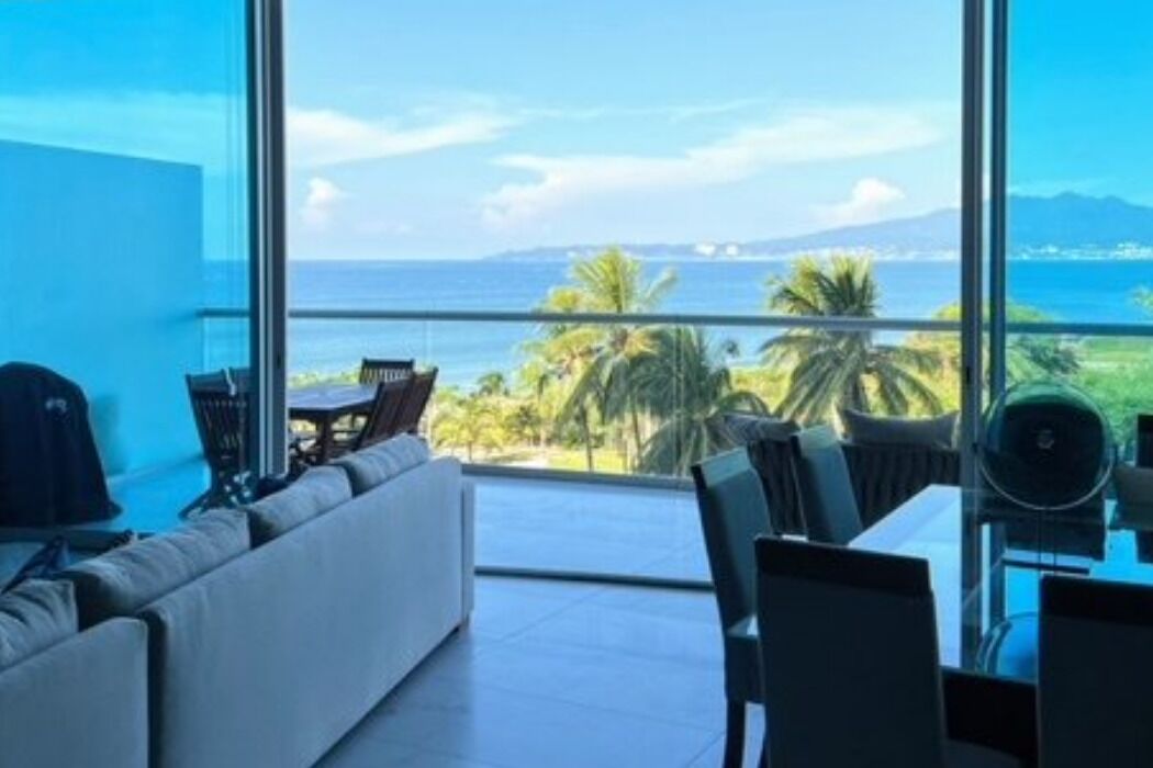 Una habitación moderna con un ventanal amplio que ofrece vistas al mar y palmeras.
