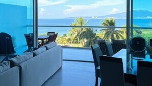 A modern room with a large window offering a view of the sea and palm trees. - Amazing Jewel Beach front Condo with great views (Bucerias/ Nuevo Vallarta)