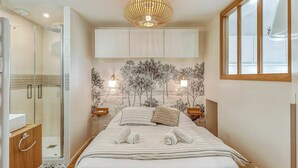 Ein modernes Schlafzimmer mit Bett, Duschkabine aus Glas, Wandregal und großem Fenster.
