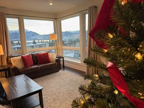 Enjoy a scenic view of snow-covered mountains from the comfort of this inviting room, featuring a cozy sofa, wooden table, and Christmas tree.