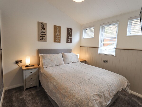 A bedroom with a bed, nightstands, a lamp, and wall art. - Jinnyspinner Lodge (Windermere)