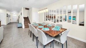 Comedor con mesa de madera dispuesta para seis, sillas blancas y una araña.