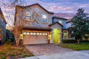 Two-story house with a garage entrance, surrounded by mature trees and well-maintained landscaping.