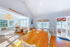 Relax in this spacious room with a high ceiling, large windows, and a dining table surrounded by comfortable seating options.