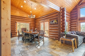 A log cabin interior with a dining area, a sofa, and a chandelier. - 0.5mi to the Lake, Deck w/ Views, Poker Table | Eagle Ridge Retreat by AvantStay (Big Bear Lake)