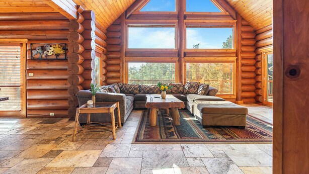 A log cabin interior with a large window, a sofa, a coffee table, and a rug.