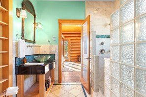 A bathroom with a wooden vanity, a glass shower enclosure, and a view into a room with a wooden floor. - 0.5mi to the Lake, Deck w/ Views, Poker Table | Eagle Ridge Retreat by AvantStay (Big Bear Lake)